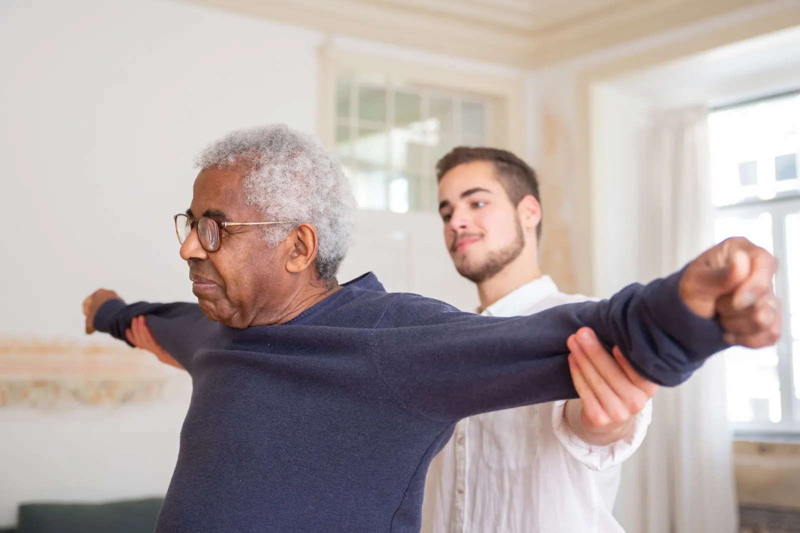 Therapist supporting an older man's arm exercise in a bright room